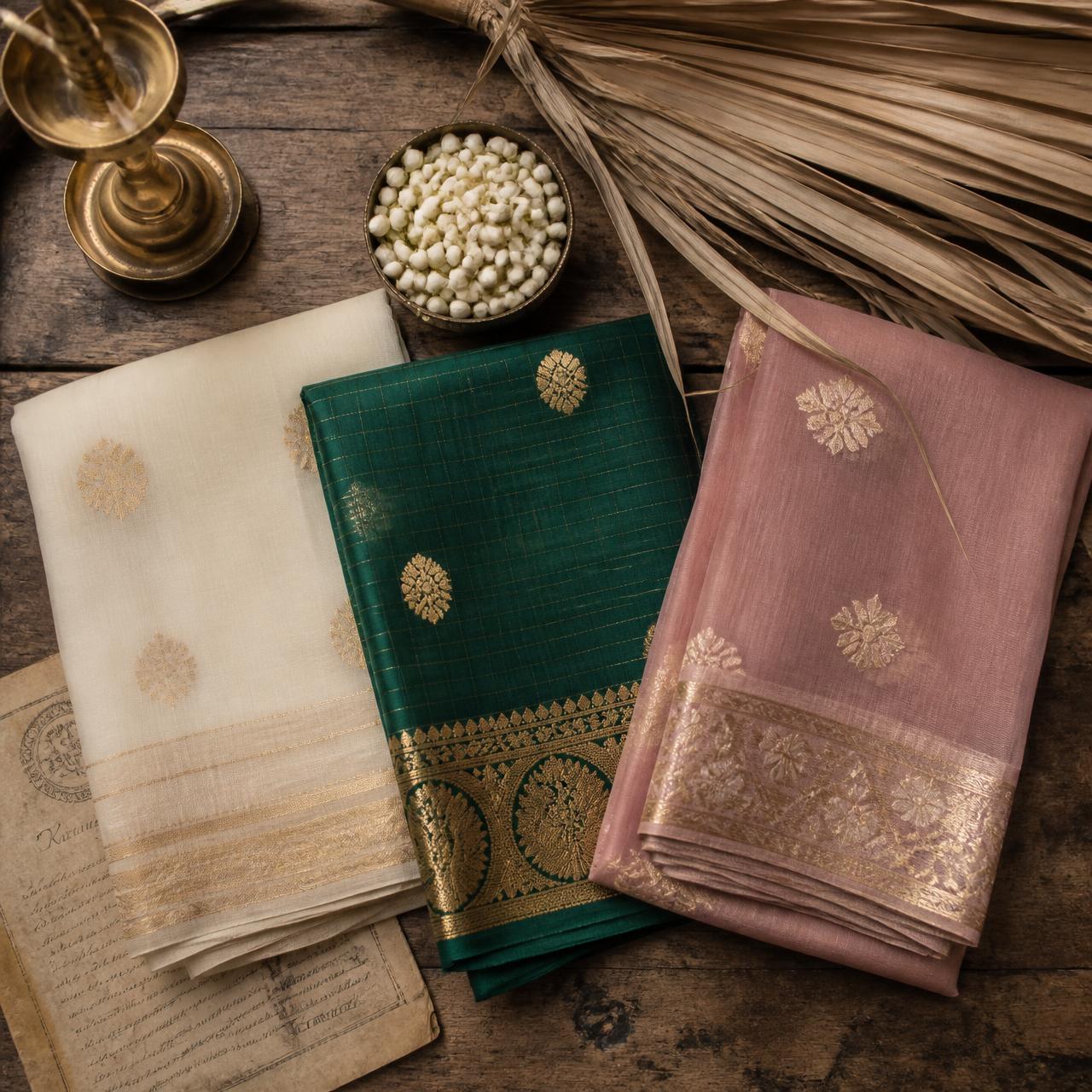 Editorial flatlay of three folded sarees with brass lamp and jasmine